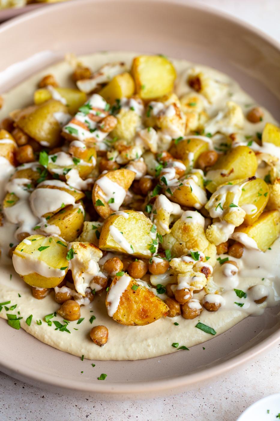 veggie bowl with roasted potato, chickpeas and cauliflower on a bed of creamy hummus and drizzled with a white tahini sauce