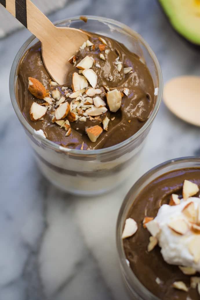 Chocolate avocado pudding in a clear glass and topped with whipped cream and nuts