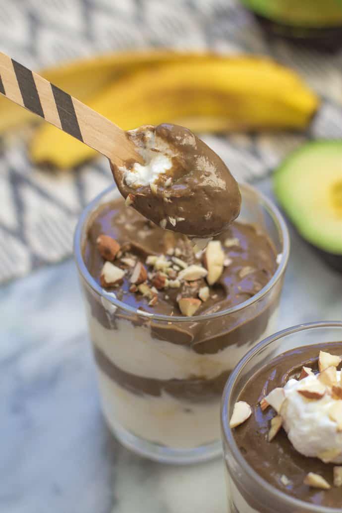 Chocolate avocado pudding in a clear glass and topped with whipped cream and nuts