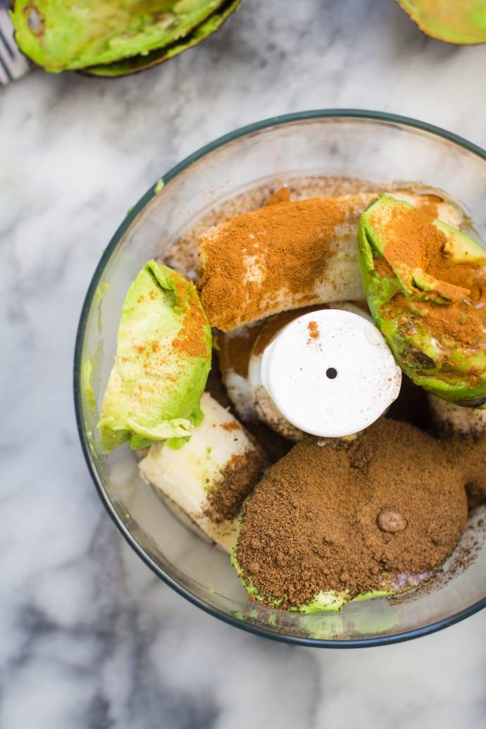 Ingredients for avocado pudding in a food processor: avocado, banana, cocoa powder