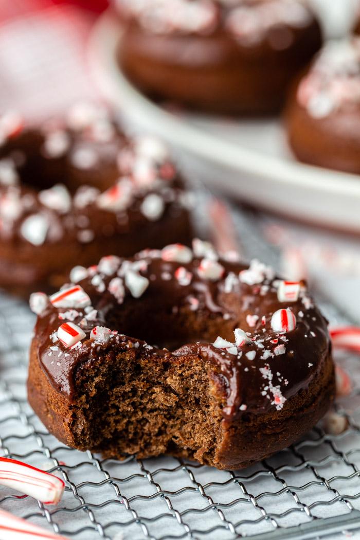 side shot of a chocolate donut topped with chocolate glaze and crushed peppermint. more of the same donuts in the background