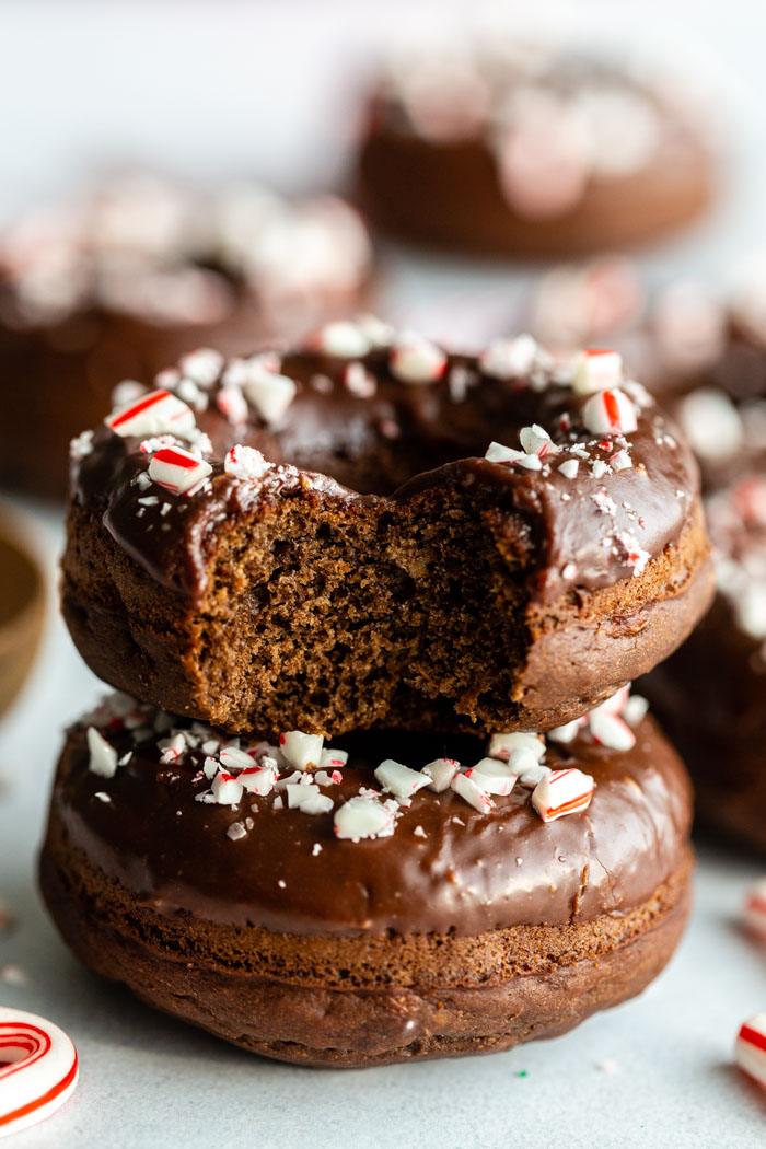chocolate peppermint donuts stacked on top of each other, one has a bite taken out of it