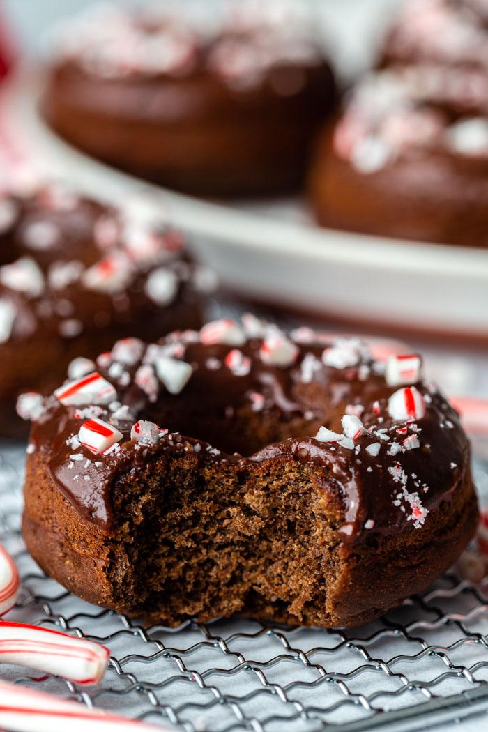side shot of a chocolate donut topped with chocolate glaze and crushed peppermint. more of the same donuts in the background