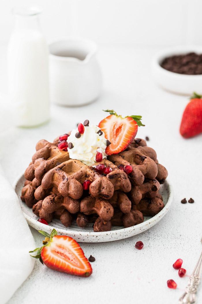 waffles stacked on a small plate topped with whipped cream and fruit