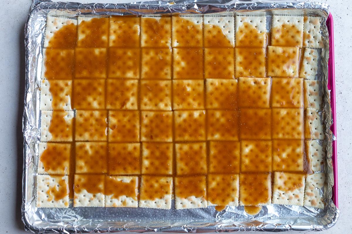 how to make christmas crack: picture showing the hot toffee poured on top of saltine crackers that are lined up on a baking tray