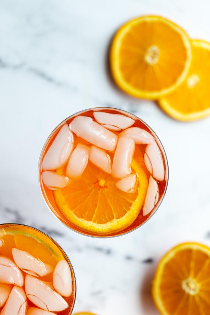orange cocktail in a wine glass on a marble backdrop with oranges all around