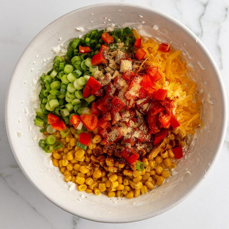 cream cheese corn dip ingredients in a bowl before being stirred including corn, bell pepper, jalapeno, cheese, and cream cheese