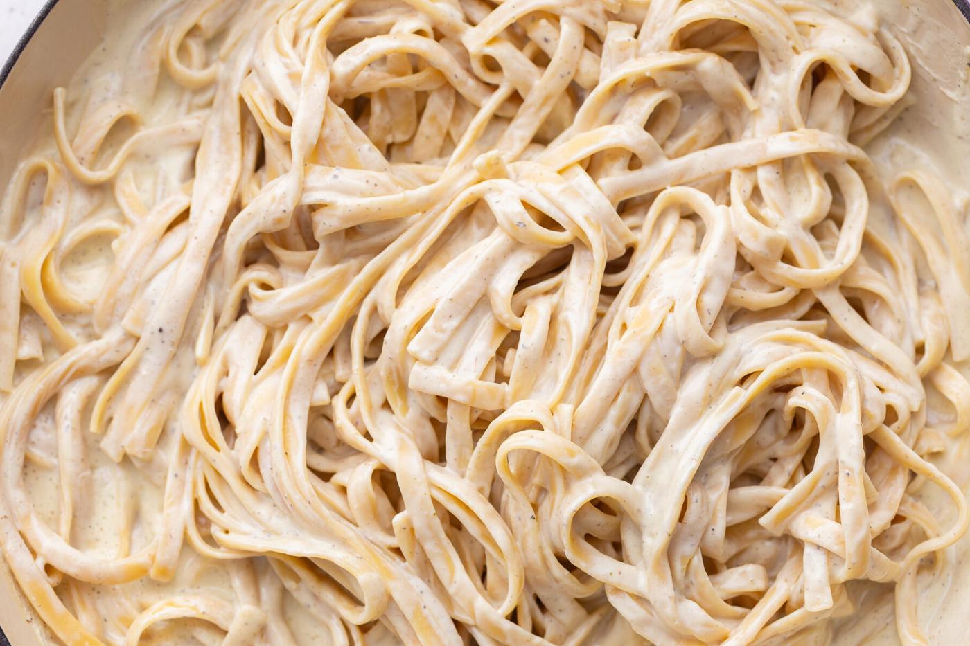 White creamy sauce tossed with pasta in a pot.