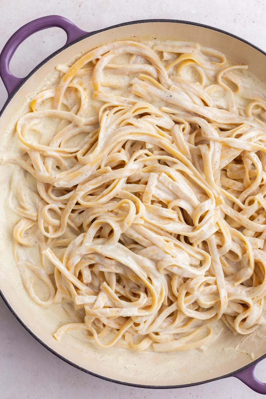 White creamy sauce tossed with pasta in a pot.