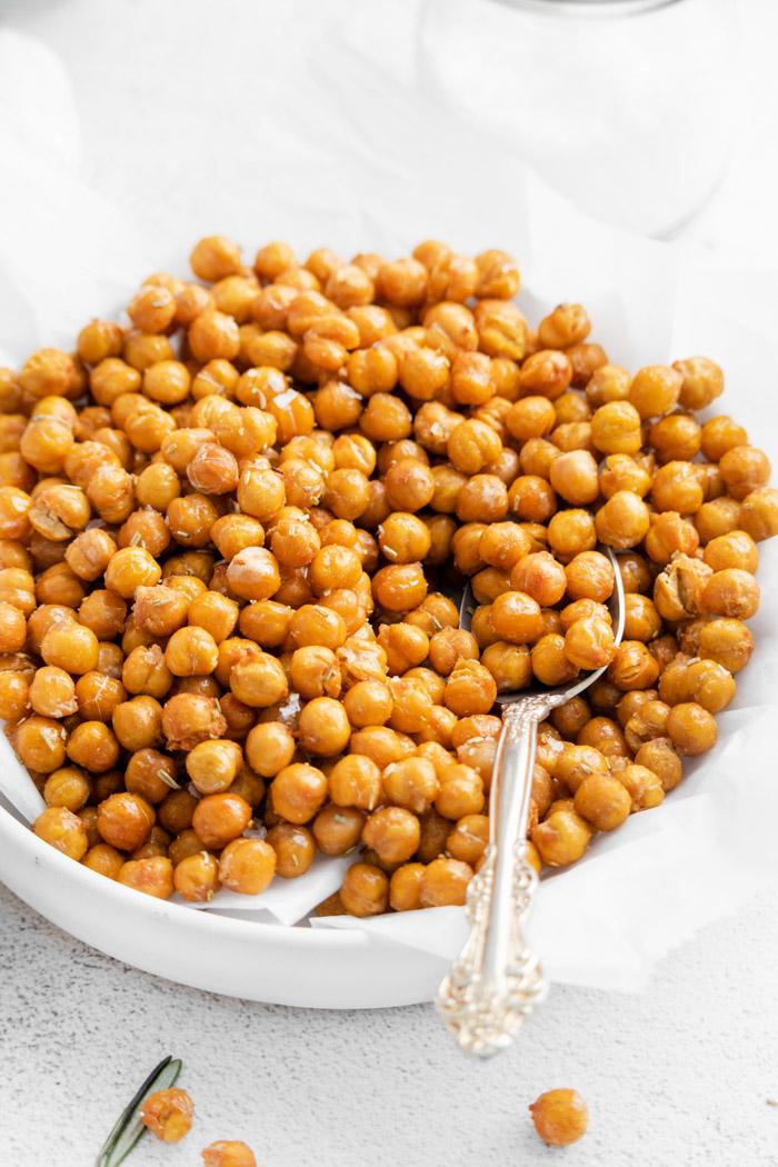 side shot of crispy chickpeas sitting in a shallow white bowl with a spoon scooping up some of the chickpeas