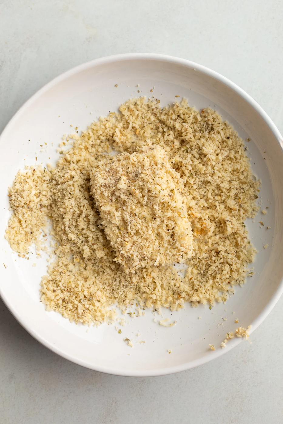 Coating a piece of tofu in breadcrumbs.
