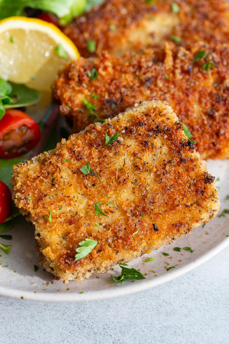 Tofu cutlets garnished with fresh parsley on a plate with a lemon wedge and salad.