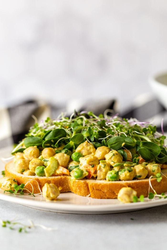 side shot of a curried chickpea sandwich topped with microgreens
