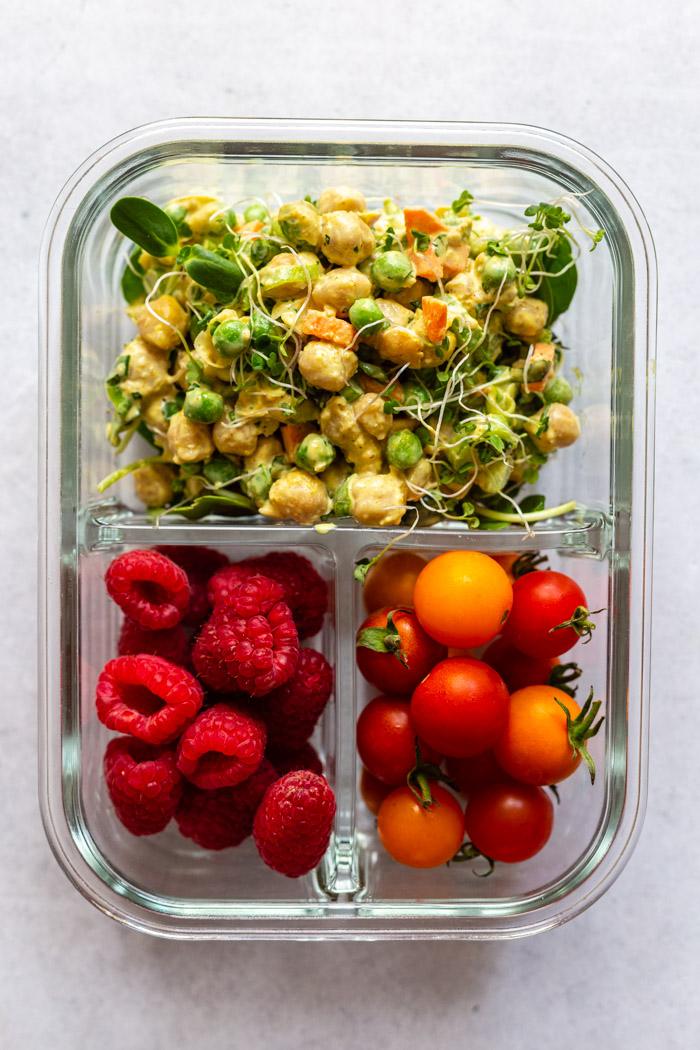 meal prep container with curried chickpea salad in the large spot, raspberries in another slot and cherry tomatoes in another