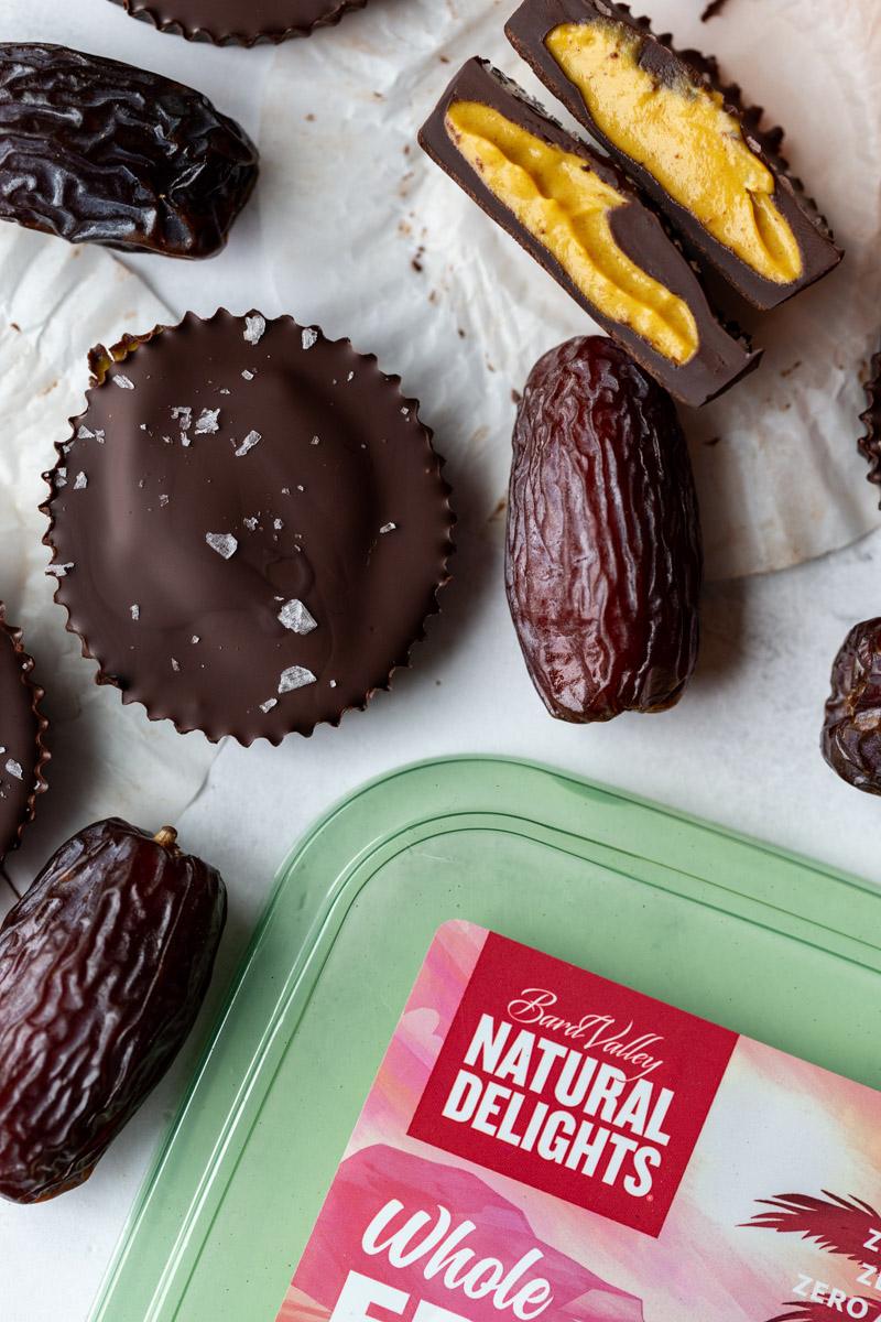 pumpkin peanut butter cups with one cut in half and a bucket of natural delight dates in the corner