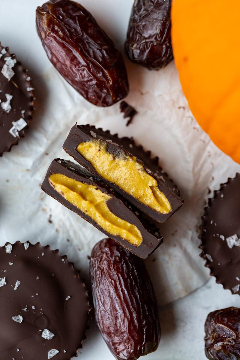 date sweetened peanut butter pumpkin cups with one cut in half and a pumpkin in the corner