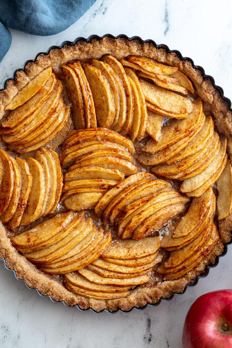 Baked apple tart on a marble board. The tart has apple arranged in groups that are going in different directions