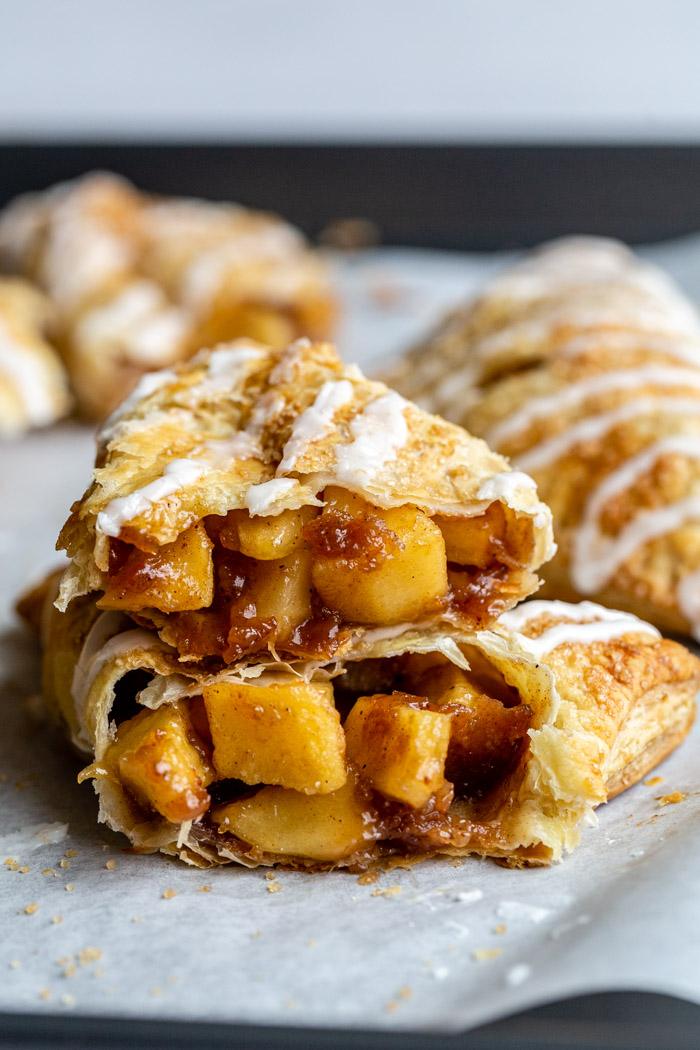 iced apple turnovers on parchment paper where you can see the inside and juicy apples