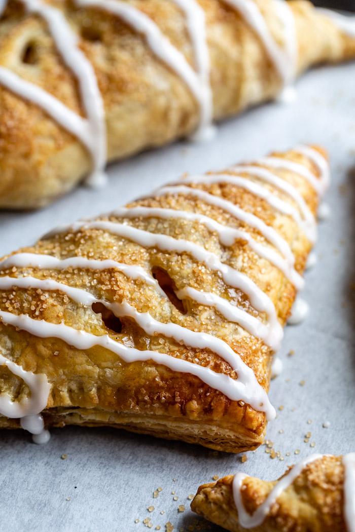 side shot of iced apple turnovers on parchment paper