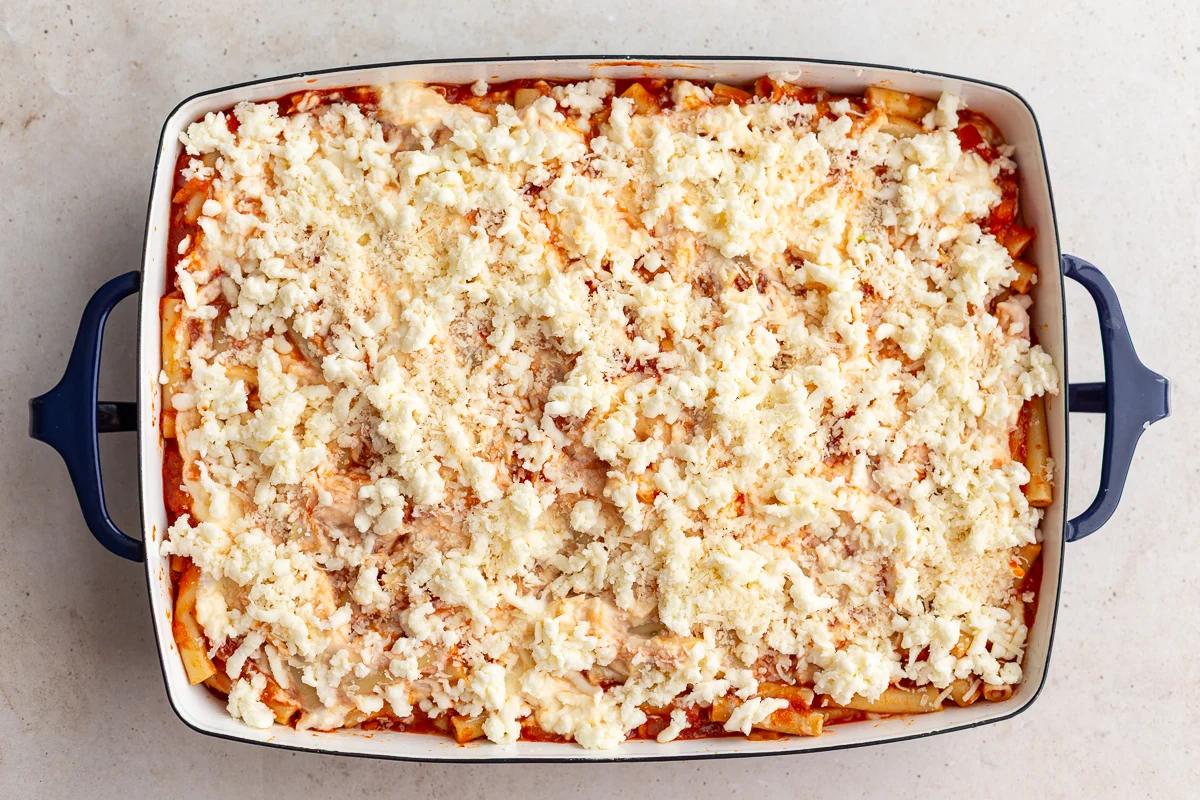 baked ziti in a casserole dish and topped with freshly grated cheese before it has been baked