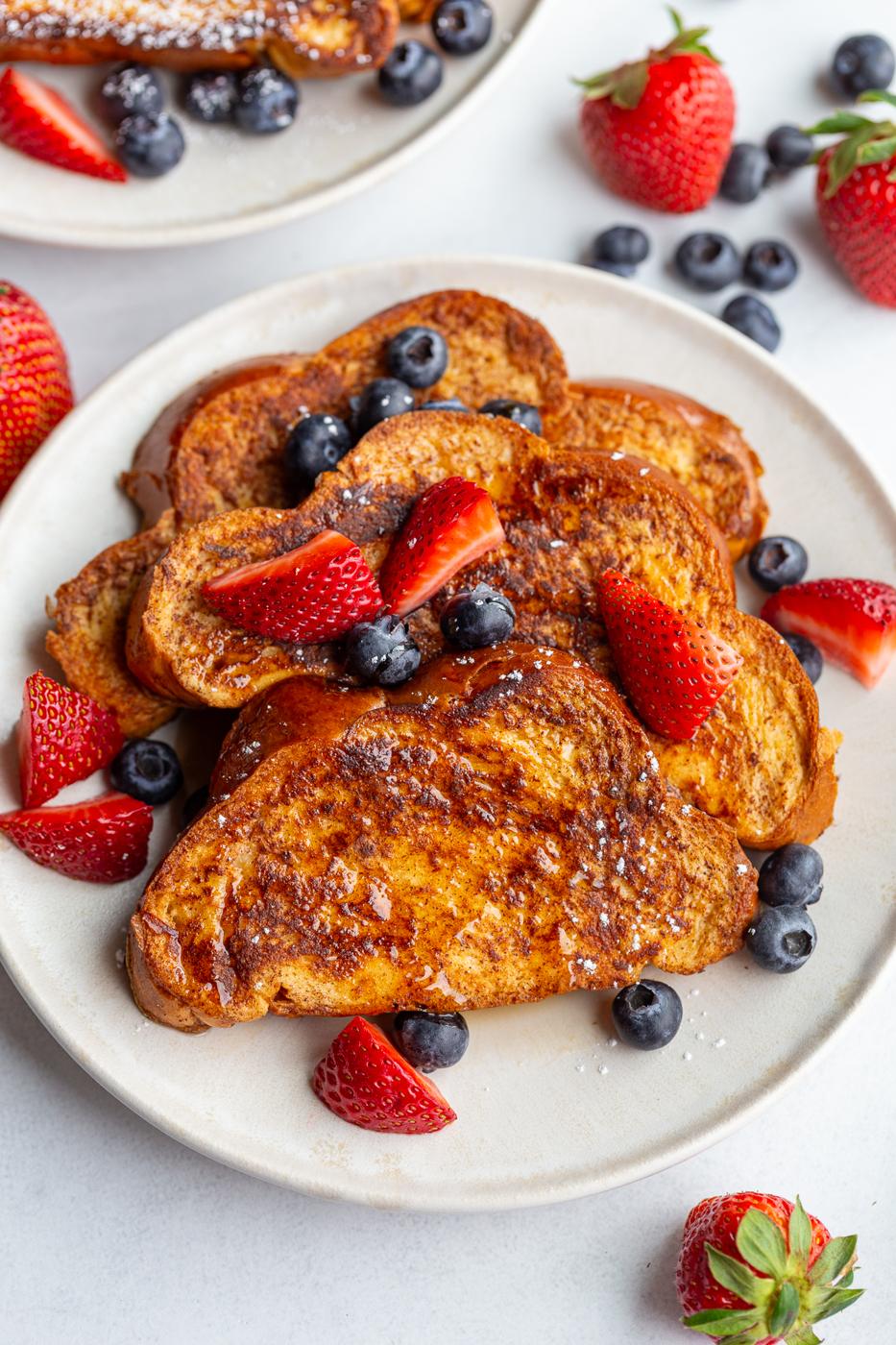 french toast on a plate with fresh strawberries and blueberries