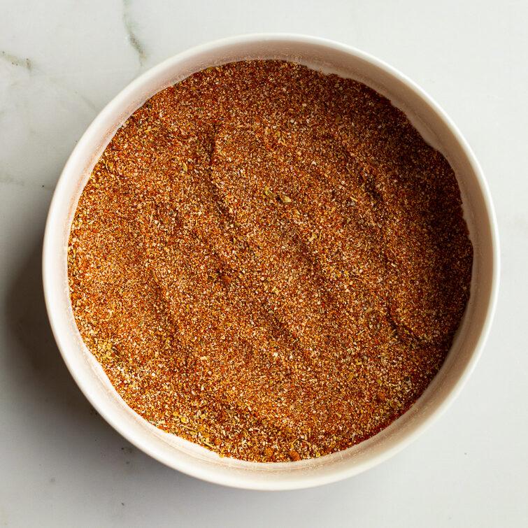 From-scratch fajita seasoning fully blended together in a white bowl on a white marble surface, showing a rich red-brown spice mixture ready to use or store.