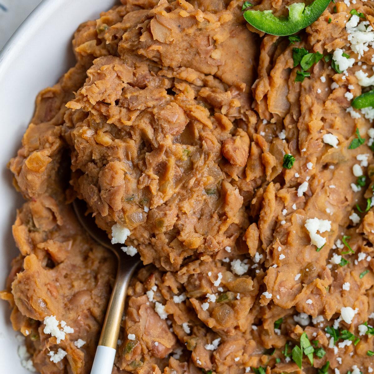 up close shot of kitchen-made refried beans with a spoon in the side and fresh jalapenos