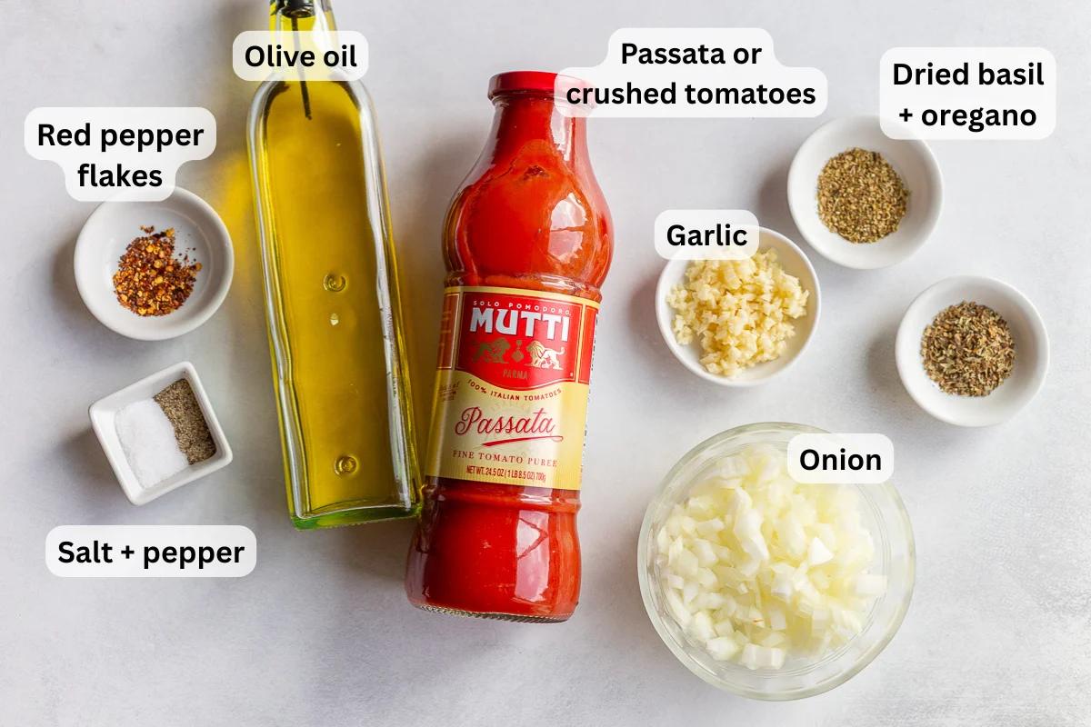 ingredients need to make from-scratch marinara sauce including passata, olive oil, spices, onion and garlic. ingredients are labeled on the image with black text