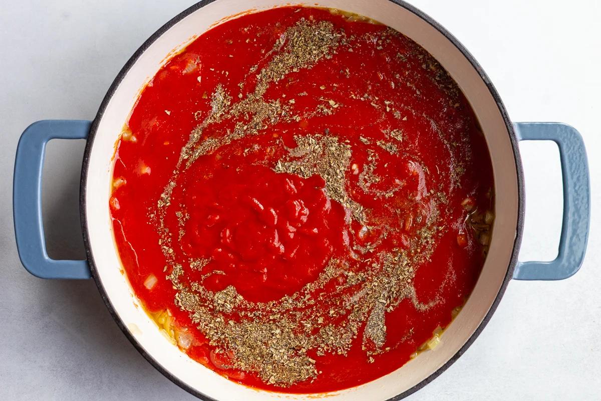 marinara sauce in a skillet with fried green herbs being mixed in