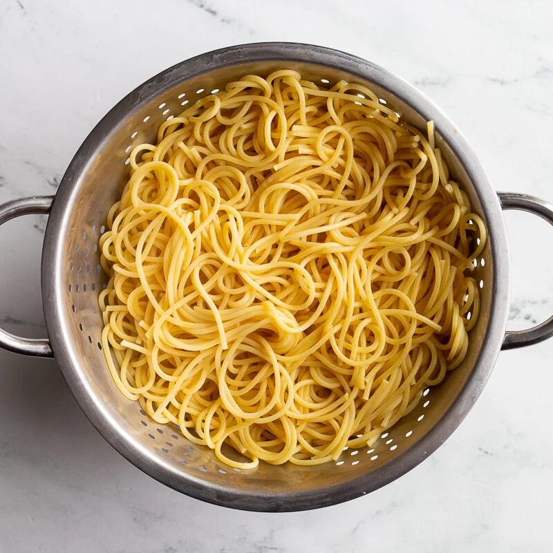 Cooked spaghetti draining in a colander.