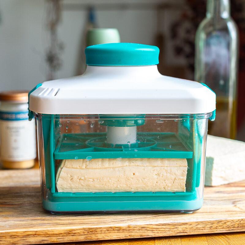 tofu in a tofu press with olive oil and soy sauce in the background