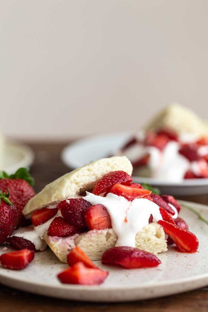 side shot of shortcake cut in half and topped with whipped cream and sliced strawberries sitting on a wooden table