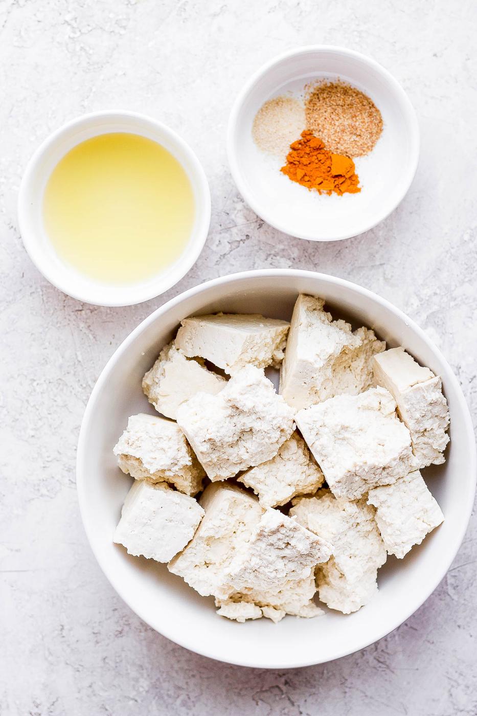 Uncooked tofu in a bowl and seasonings mixed in a separate bowl.