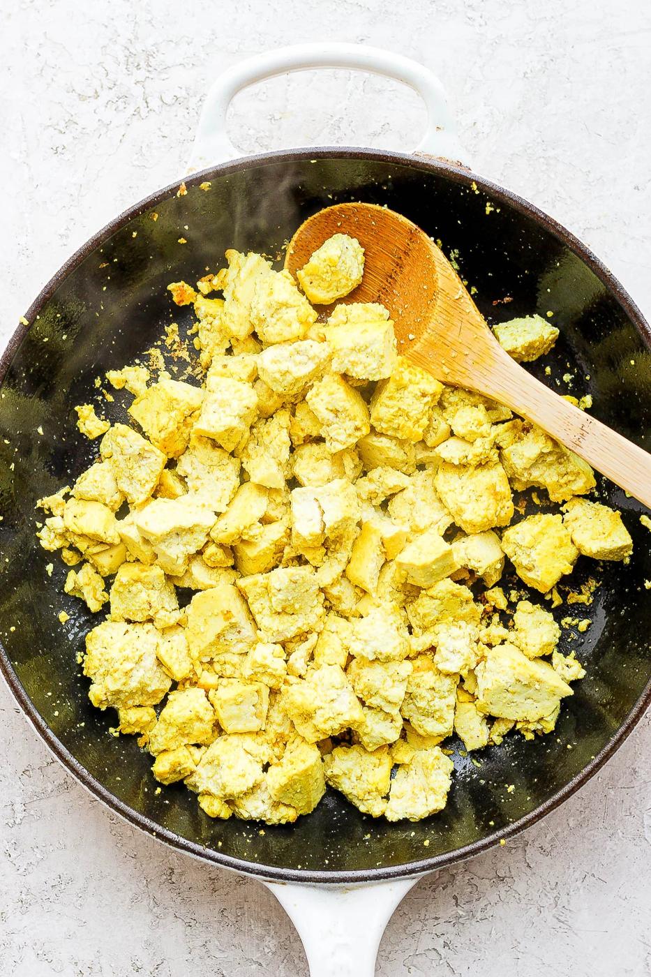 Using a wooden spoon to crumble tofu in a pan.
