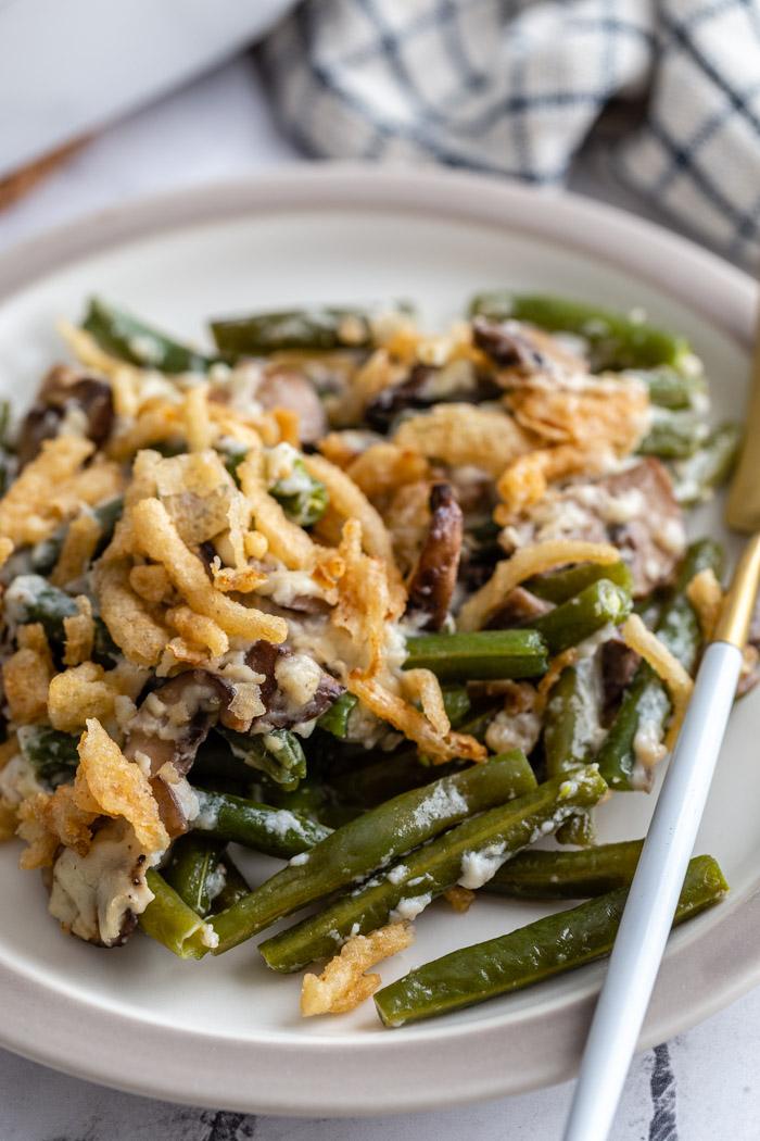 green bean casserole on a plate topped with fried onions. a scoop full being taken out
