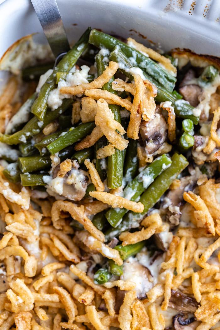 green bean casserole in a baking dish topped with fried onions. a scoop full being taken out