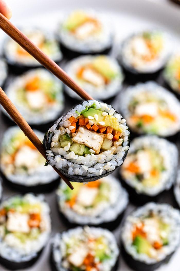 sushi slice being held up to the camera with more in the background