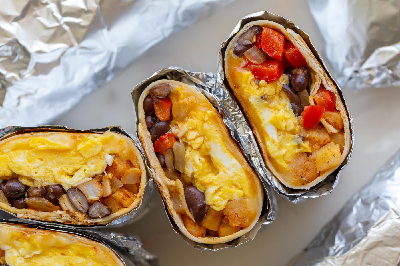 unfussy breakfast burrito recipe with 2 burritos cut open so you can seethe eggs, veggies and black beans inside