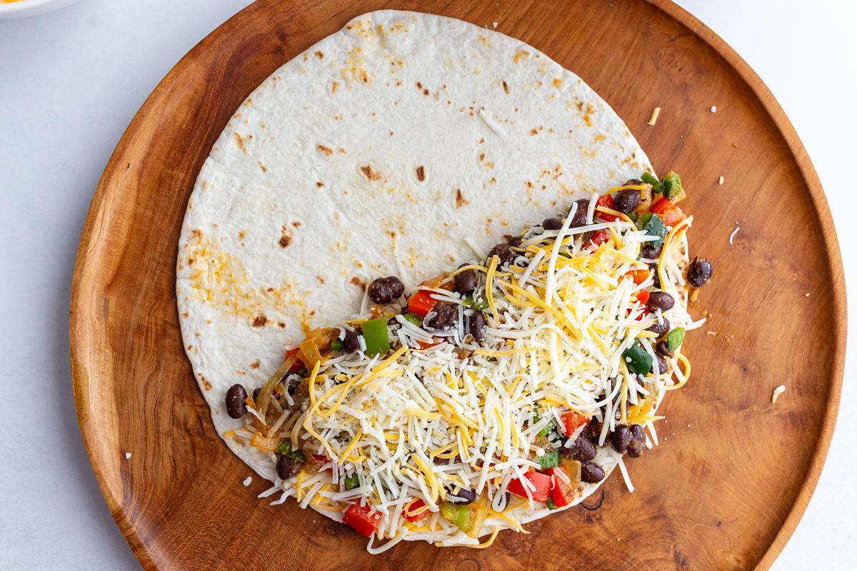 uncooked quesadilla on a wood board so you can see the bean mixture + cheese inside