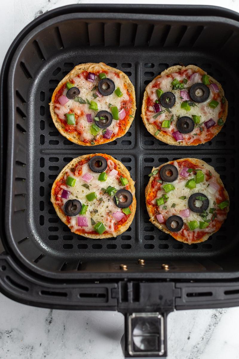 english muffin veggie pizzas sitting in an air fryer fully cooked