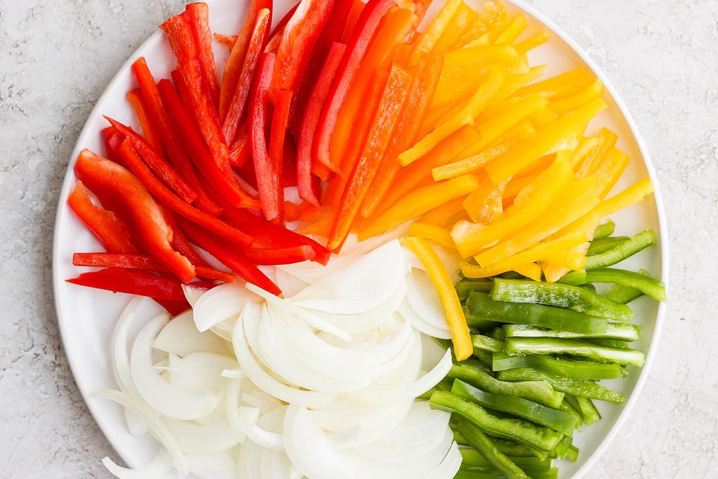 Colorful sliced bell peppers and onion on a white plate.