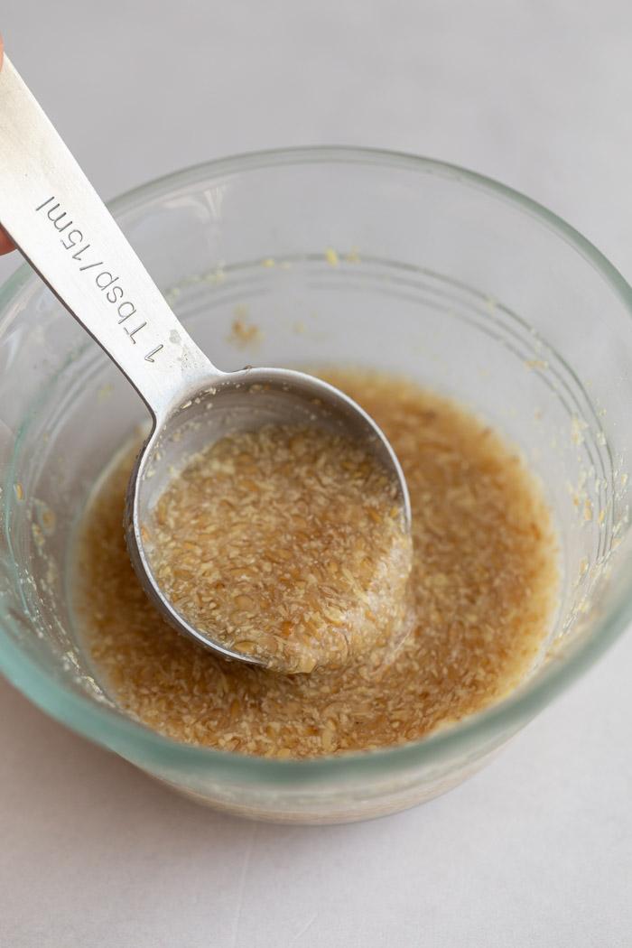 flax egg in a glass bowl with a metal spoon scooping some out