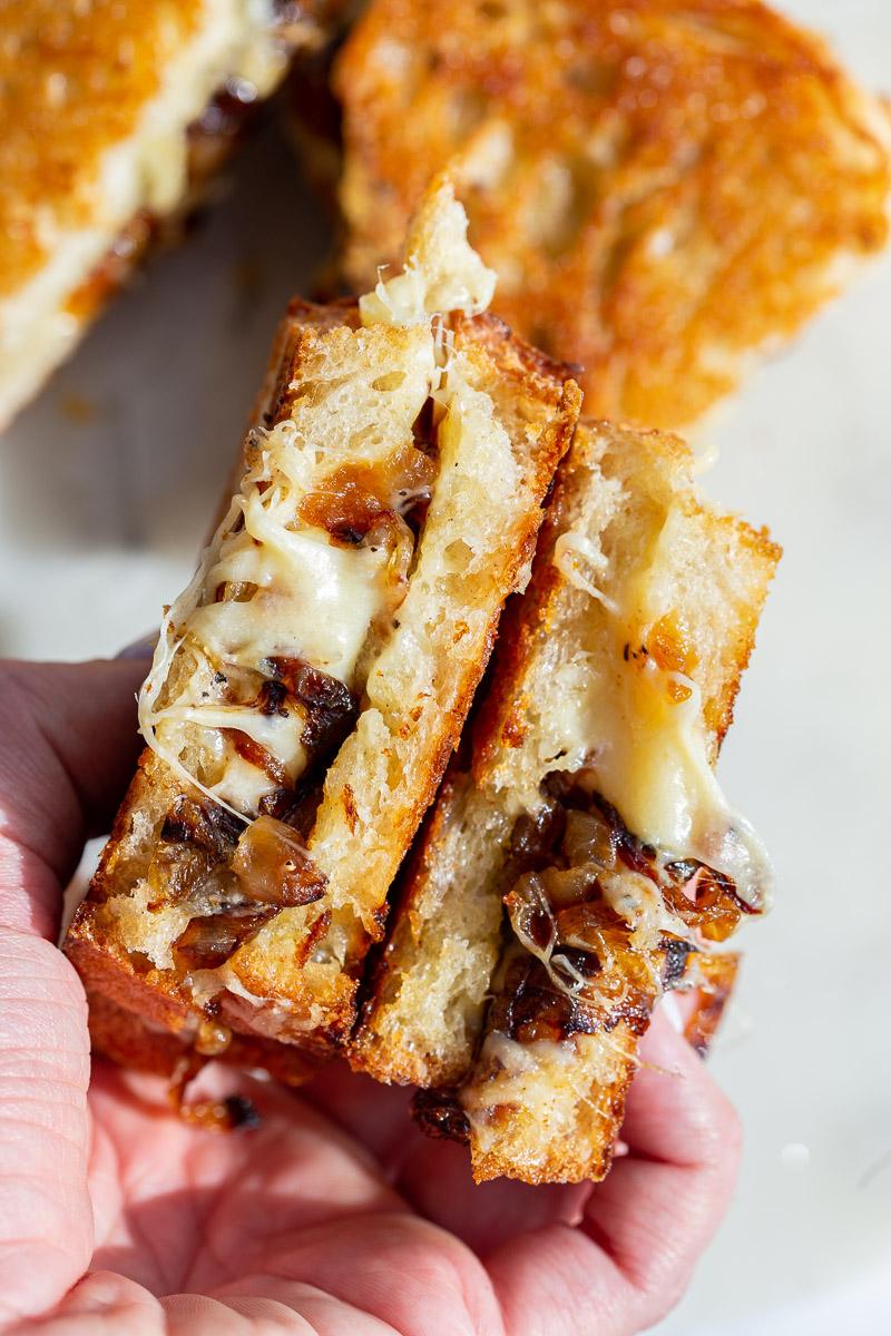 Caramelized Onion grilled cheese held in a hand with cheese and onion oozing out