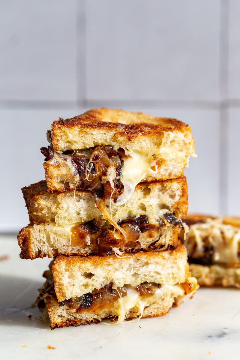 Caramelized Onion grilled cheese stacked on top of itself with cheese and onion oozing out