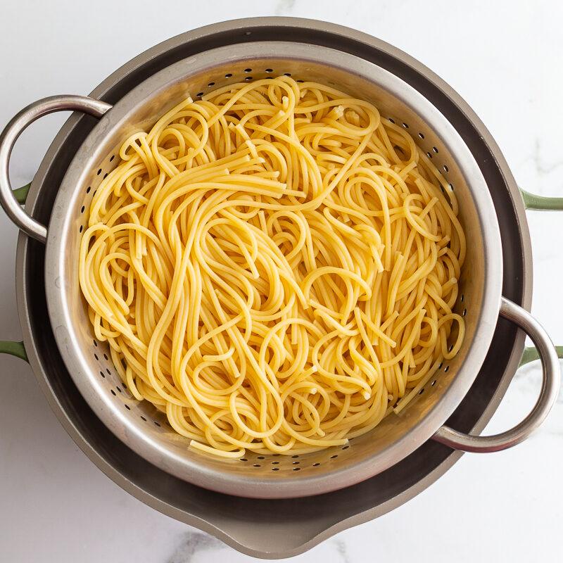 Cooked spaghetti noodles draining in a colander after boiling.