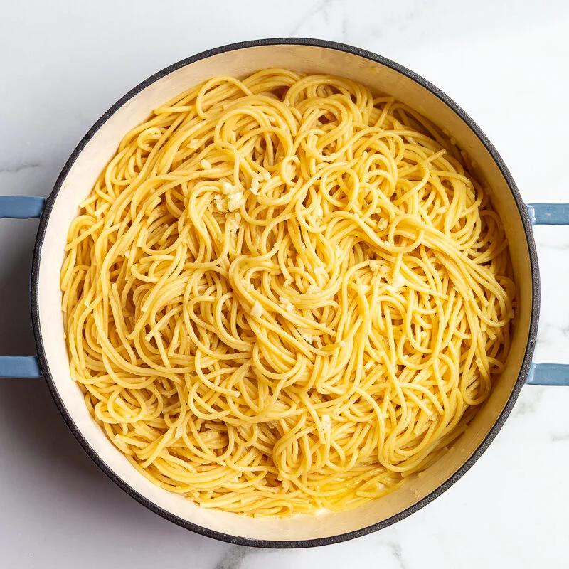 Spaghetti tossed in garlic butter and parmesan in a large pot, ready to serve.