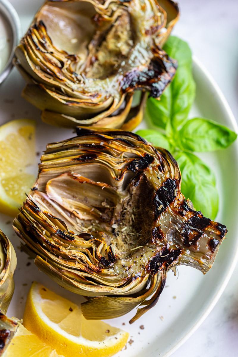large plate with 4 grilled artichokes on it and lemon slices on the plate