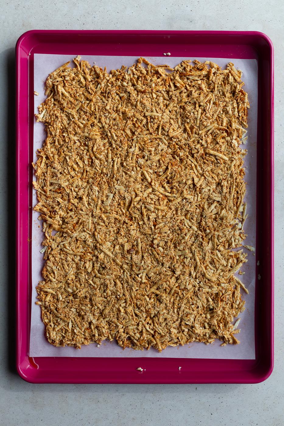 shredded tofu tossed with olive oil and taco seasoning on a large red baking sheet
