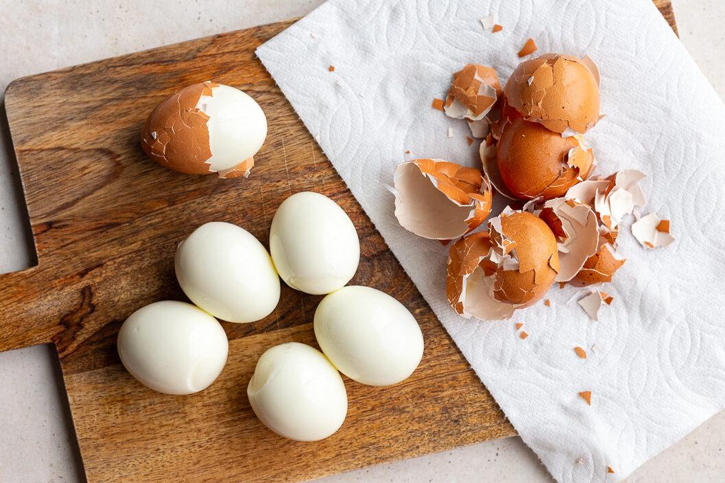 hard boiled eggs half peeled on a cutting board