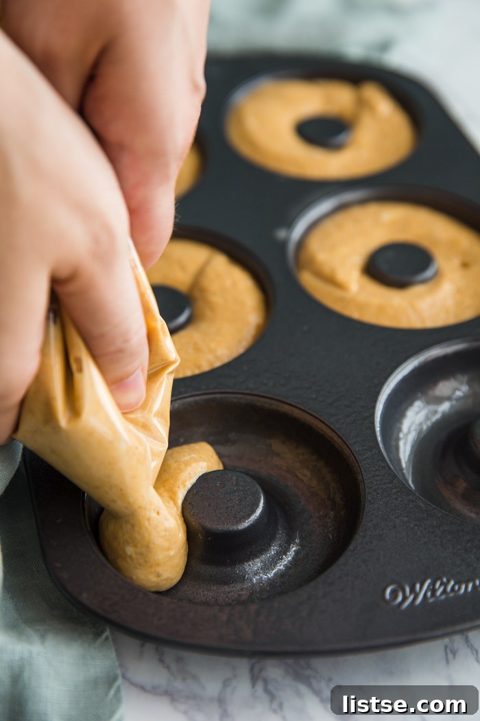 Spiced Pumpkin Donut Delights 6 Pumpkin donut batter being piped into a non-stick donut pan.